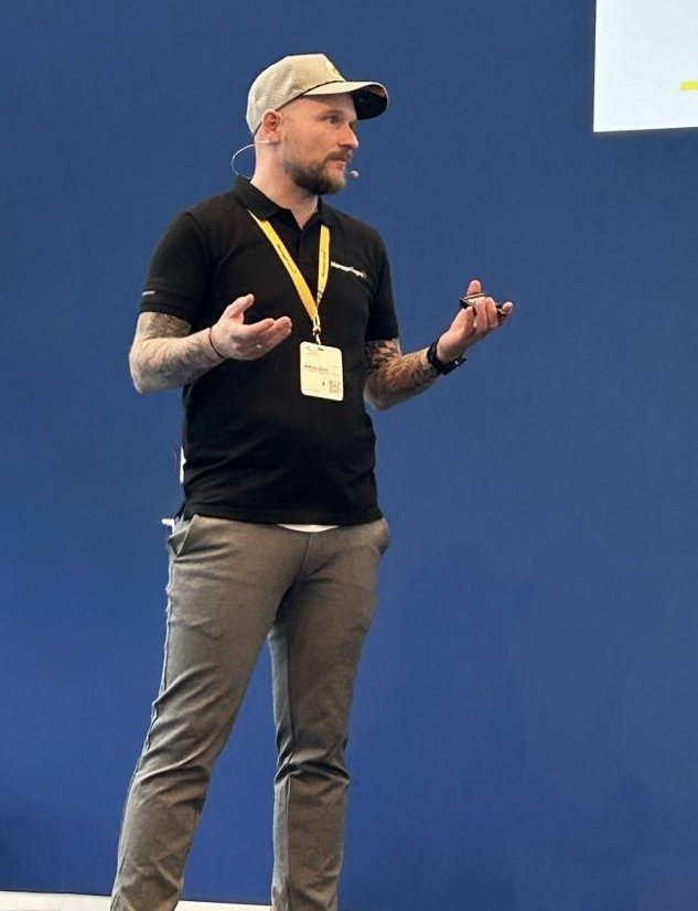 Andreas Klare bei einem Vortrag, mit Headset-Mikrofon vor blauer Bühnenwand.